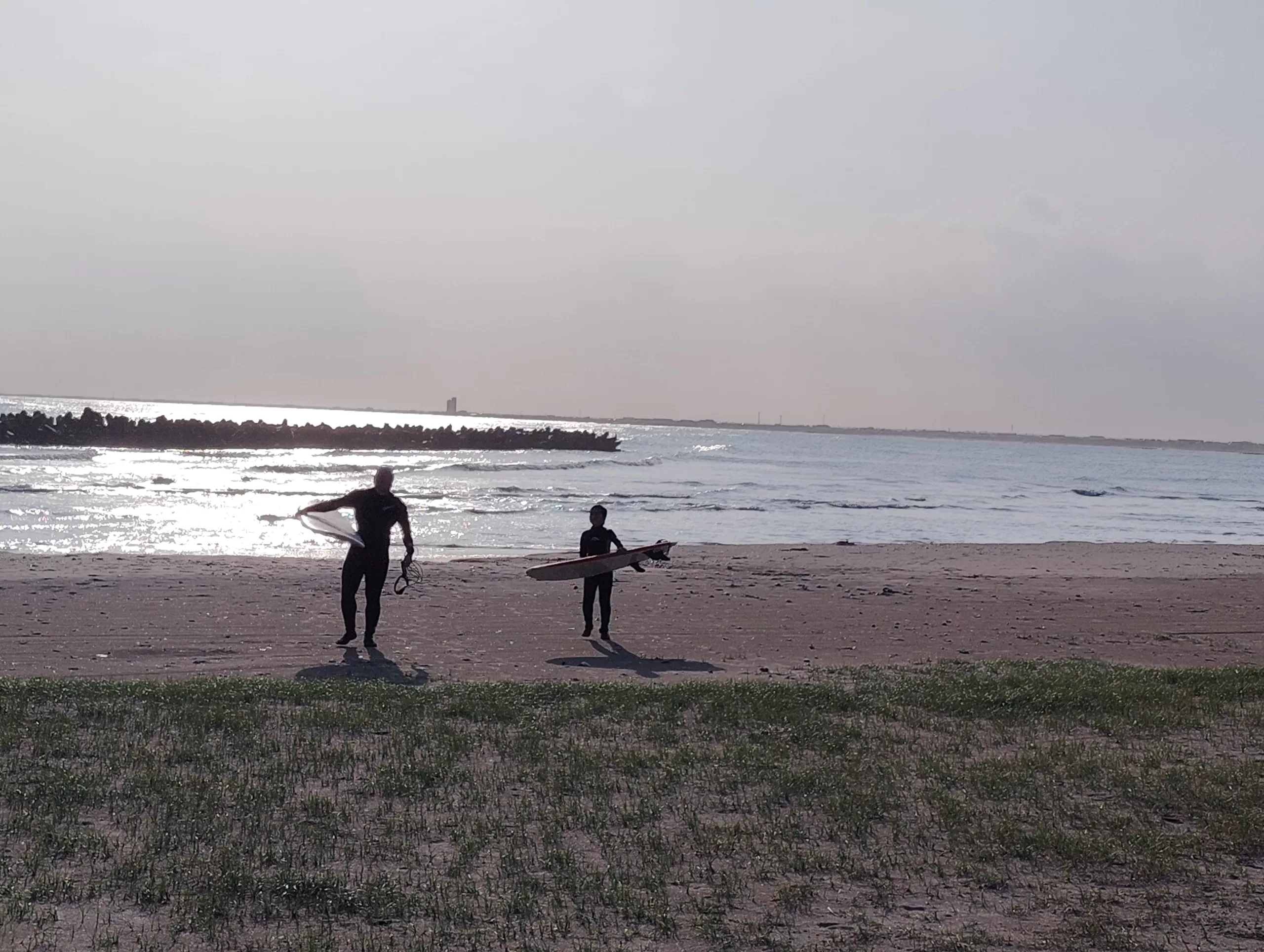 午後の海でサーフィンを終えた親子が浜辺を歩く風景